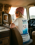 Person sitting inside a van wearing a 'Tandem Surf' t-shirt and pink beanie.